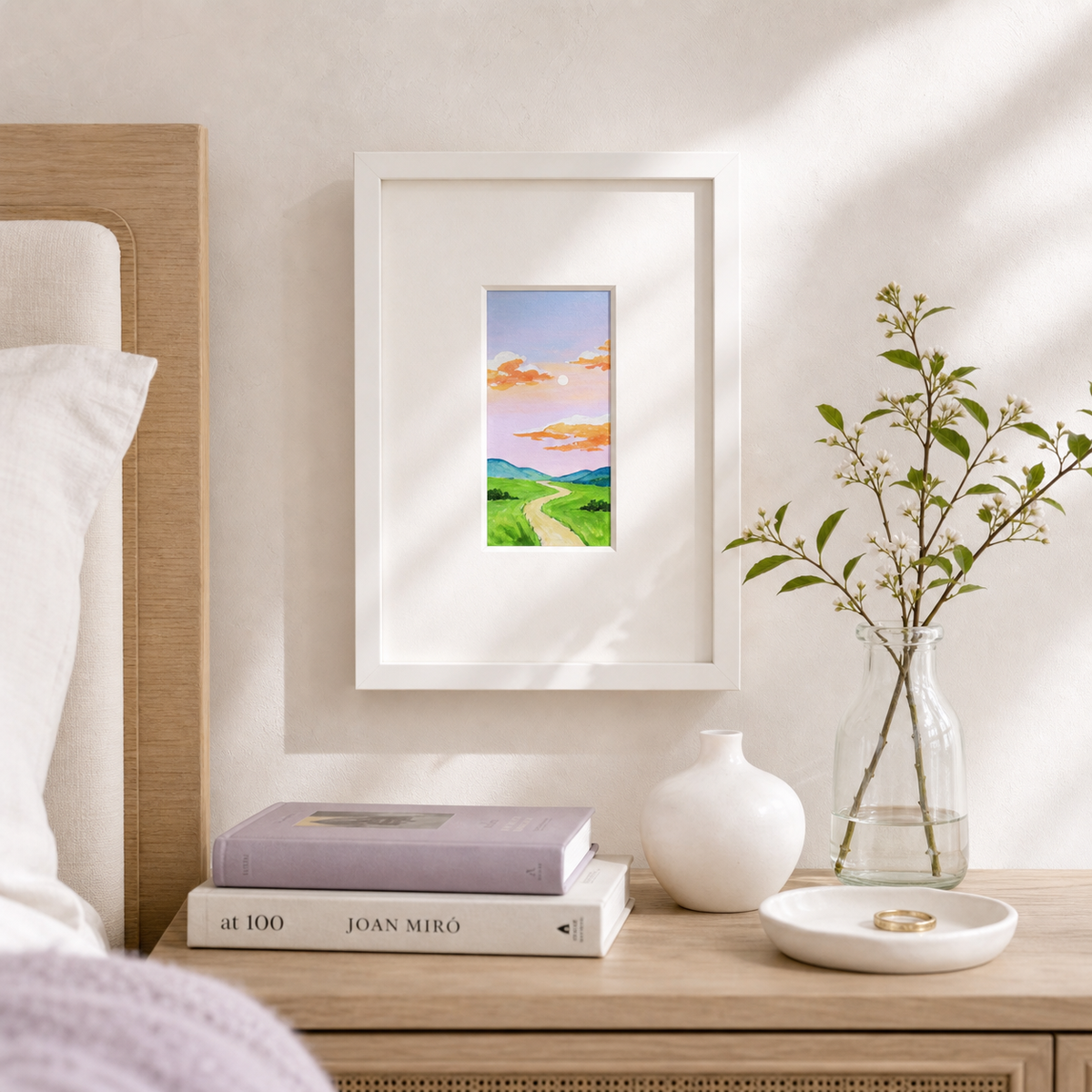 Purple Sunset by Amber Miro, original tiny painting of a purple and pink sky, framed on a nightstand beside books