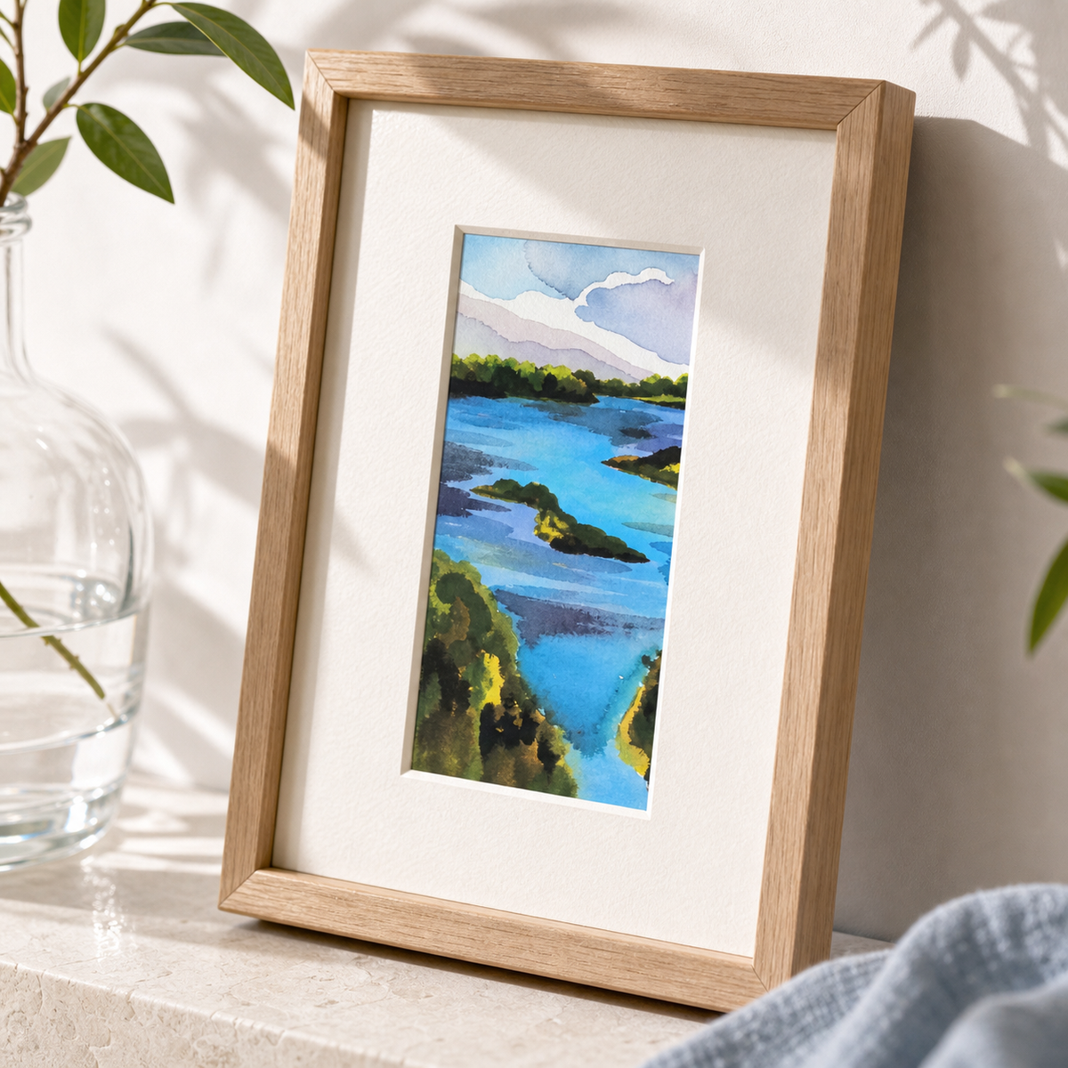 Damariscotta by Amber Miro, original coastal watercolor in deep blue and sand, angled view in an oak frame with white mat