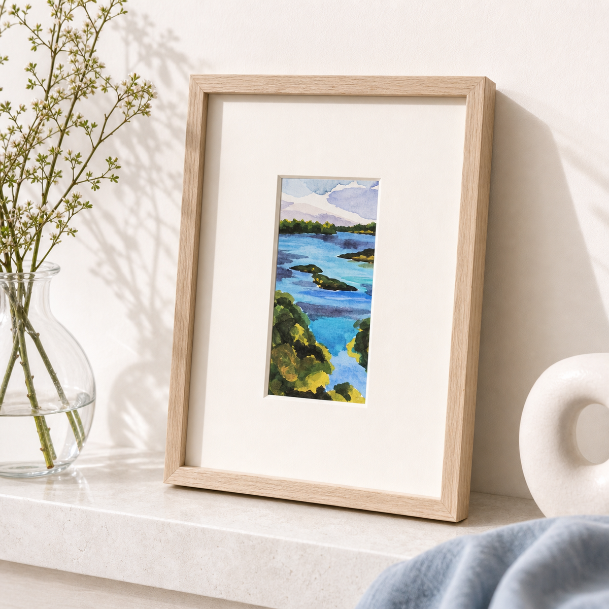 Damariscotta by Amber Miro, original coastal watercolor in deep blue and sand, matted in oak, leaning on a white shelf