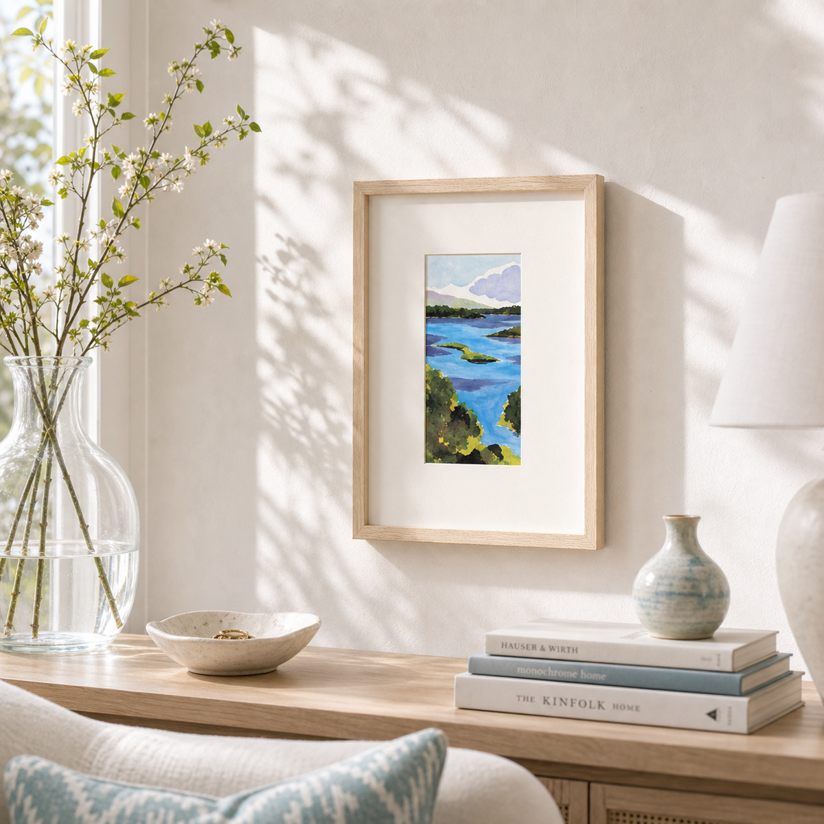 Damariscotta by Amber Miro, original coastal watercolor in deep blue and sand, framed above a wooden console with books