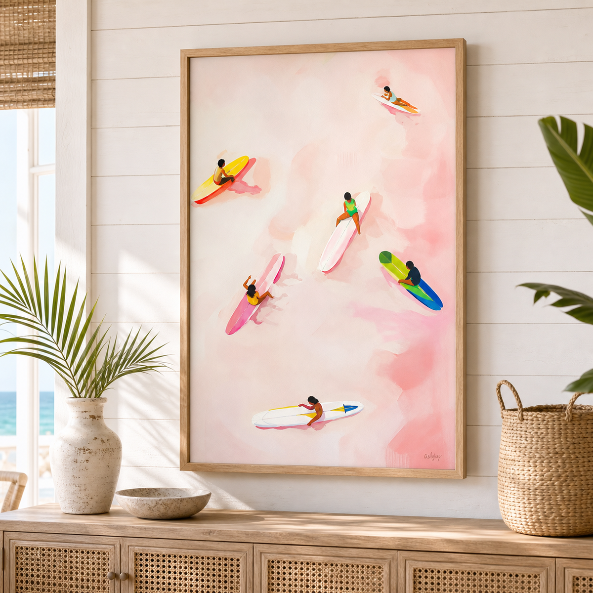 Pink Surf by Amber Miro, original painting of surfers on a pink and coral wash, framed above a rattan sideboard